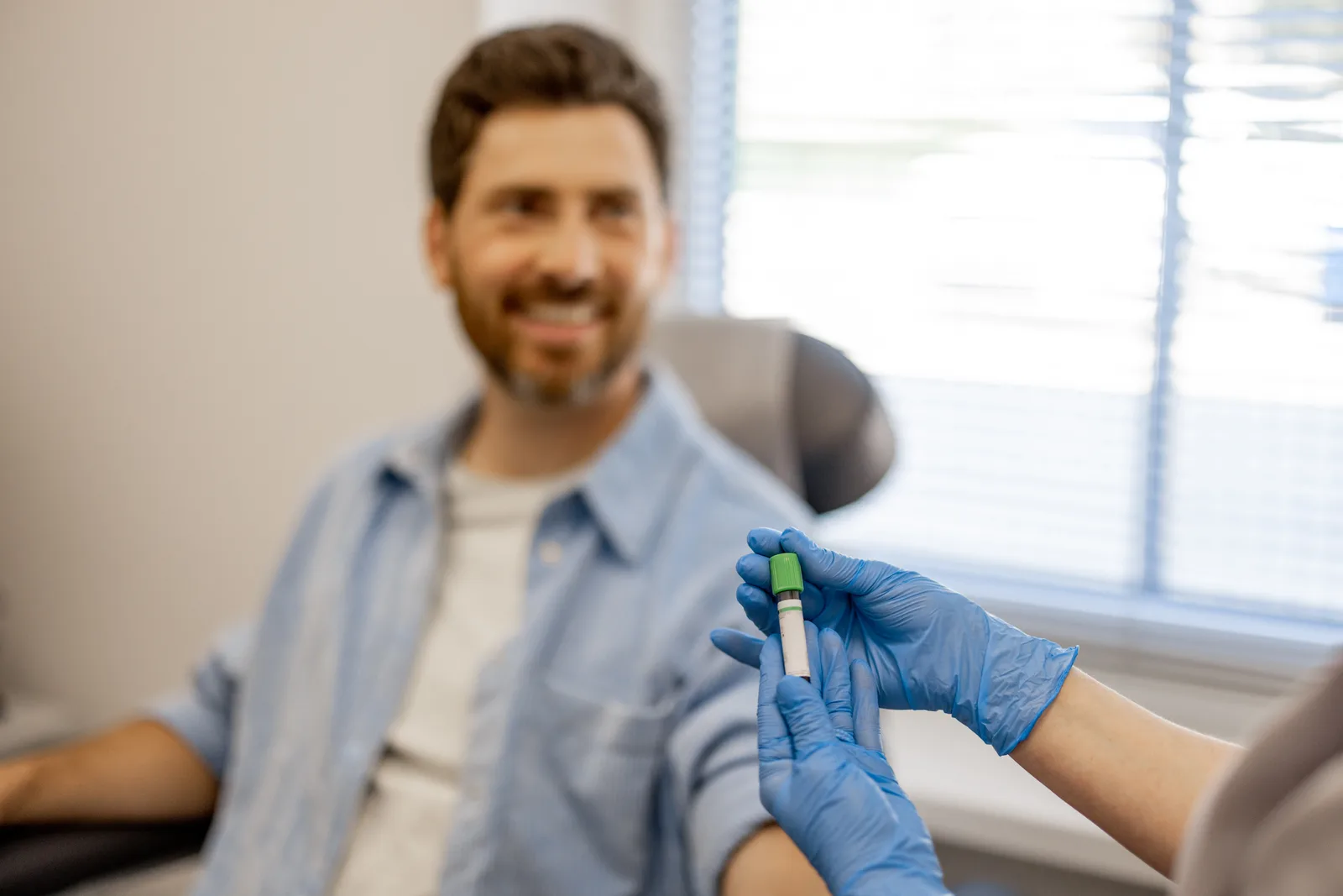 A clinician holding a blood sample tube, with a patient seated in the background.