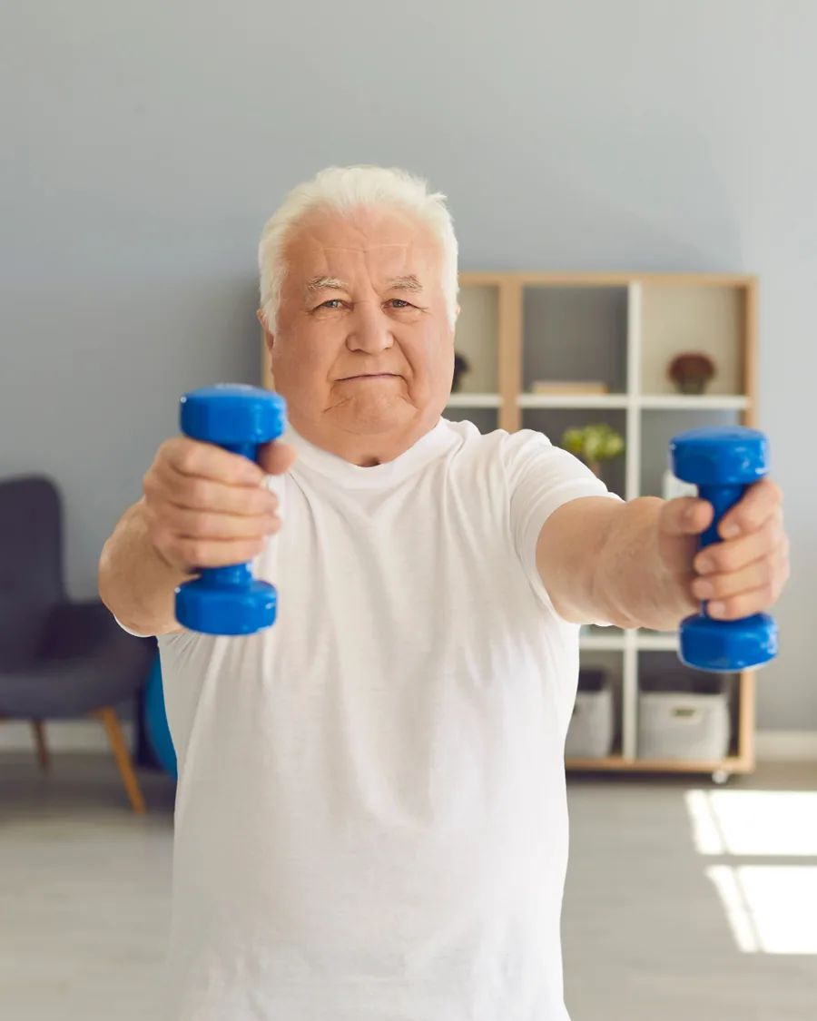 An older man lifting light dumbbells at home.