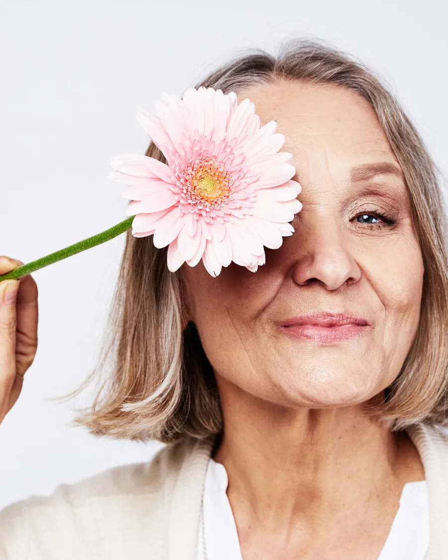 A woman in her sixties holding a gerbera daisy, smiling.