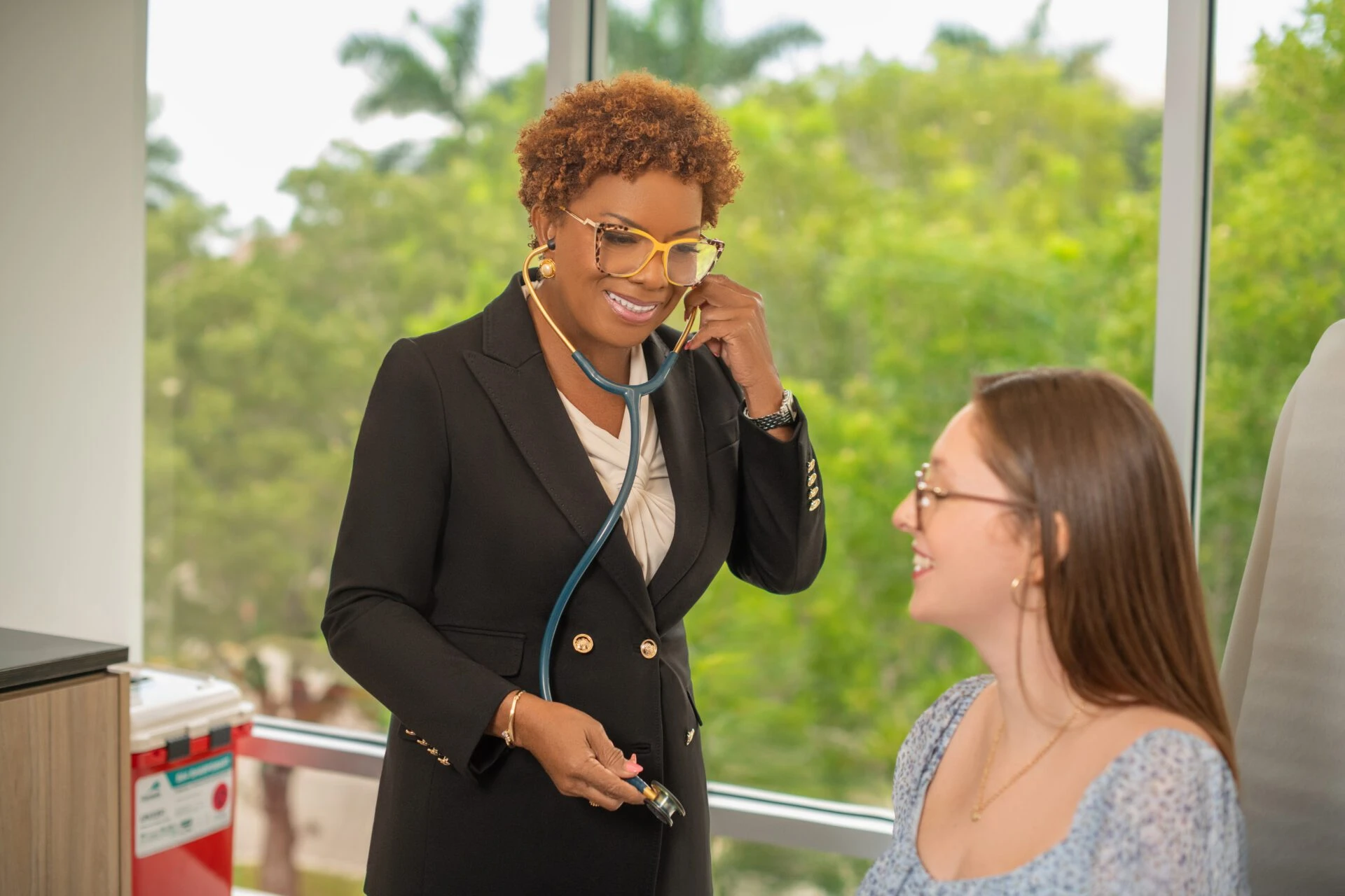 A woman sits on a couch while discussing her health with a doctor in a professional setting.