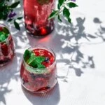 A sparkling blueberry and blackberry mocktail garnished with fresh mint and peach slices, representing a healthy 4th of July recipe from Naples Concierge Health.
