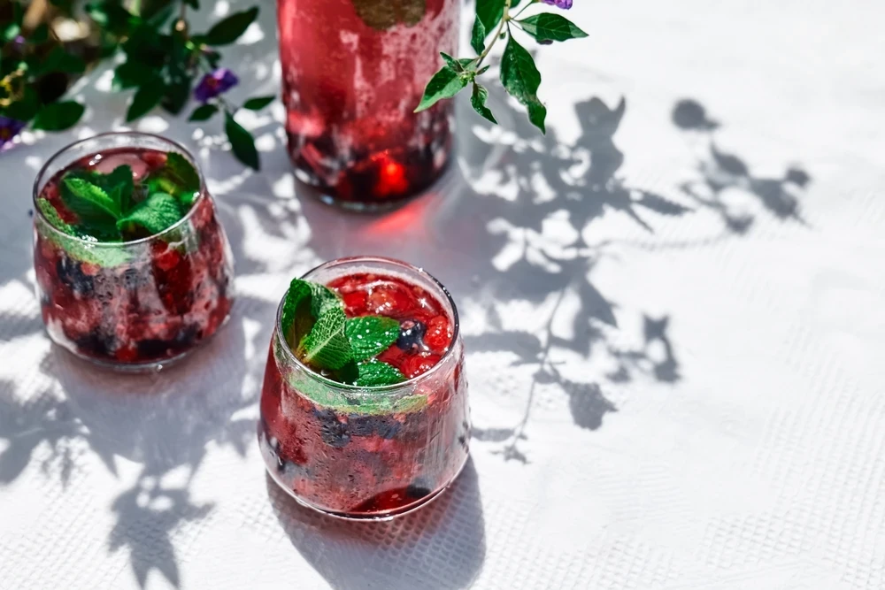 A sparkling blueberry and blackberry mocktail garnished with fresh mint and peach slices, representing a healthy 4th of July recipe from Naples Concierge Health.